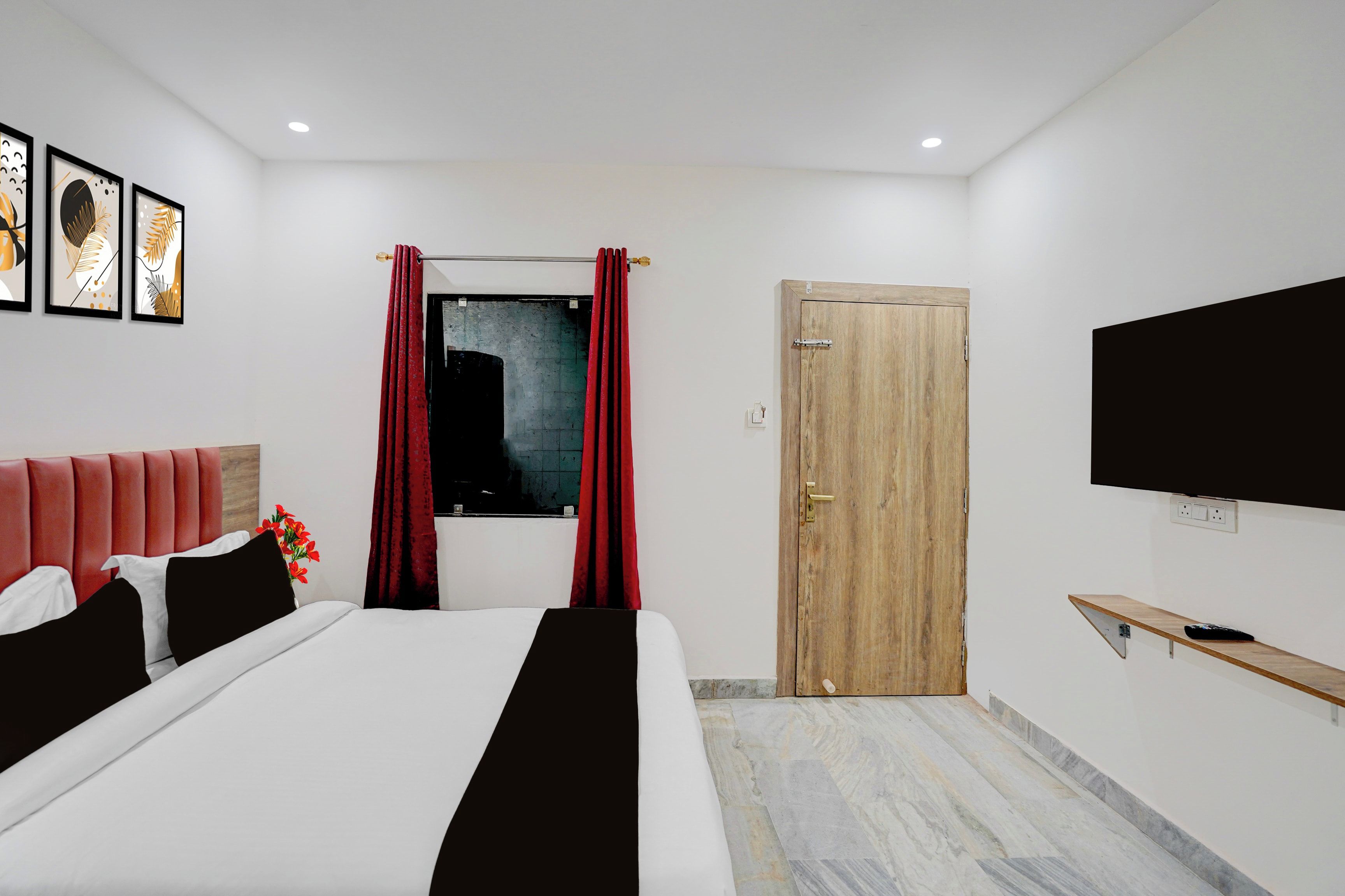 A modern hotel room with a bed, a TV, a wooden door, and a window with red curtains.