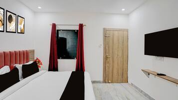 A modern hotel room with a bed, a TV, a wooden door, and a window with red curtains.