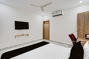 Habitación de hotel con una cama, televisión, aire acondicionado, puerta de madera y una silla.