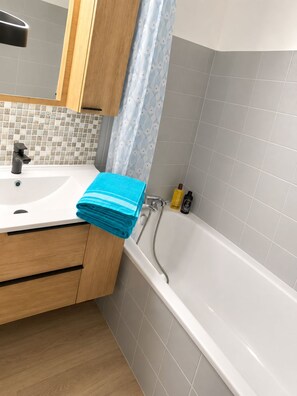 A bathroom with a white sink, wooden cabinets, a blue towel, and a bathtub. - Mountain views in the heart of the slopes, with a balcony, Wi-Fi, and a parking space. (Métabief)