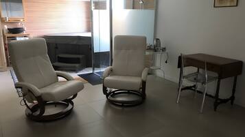 A modern living room with two reclining chairs, a small table, and a glass shower enclosure.