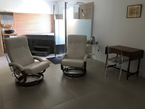 A modern living room with two reclining chairs, a small table, and a glass shower enclosure.