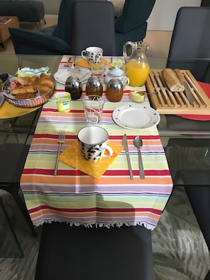A breakfast table set with plates, cutlery, a jug of orange juice, a basket of croissants, and a pitcher of tea. - Bed and Breakfast 'Le Pas Des Chevreuils' with Wi-Fi (Salles)