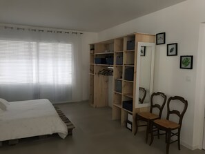 Un dormitorio con una cama, un armario de madera, dos sillas y una ventana con persianas.