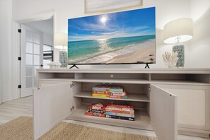Ein Fernseher auf einem Schrank mit einer Strandansicht, einer Lampe und Brettspielen auf Regalen.