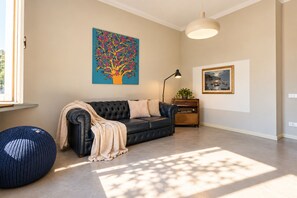 A living room with a black leather sofa, a blue knitted pouf, a painting of a tree, and a lamp. - Frontemura House with a Terrace (Lucca)