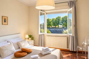 A hotel room with a bed, a window with a view of trees, a bedside table with a lamp, and a clear chair. - Frontemura House with a Terrace (Lucca)