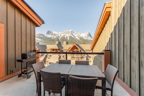 A balcony with a table and chairs, a grill, and a view of mountains. - Mountain Eye Candy | Penthouse with Pool and Hot Tub (Canmore)