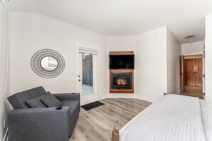 A room with a grey sofa, a bed, a fireplace, and a TV mounted on the wall. - Mountain Eye Candy | Penthouse with Pool and Hot Tub (Canmore)
