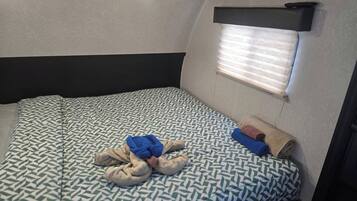 A compact bed with a patterned bedspread, a window with blinds, and a television mounted above the bed.