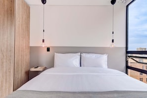Ein Hotelzimmer mit einem großen Bett, zwei Nachttischen, einem Beistelltisch und Blick auf die Stadt durch ein Fenster.
