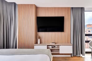A modern bedroom with a large bed, a flat-screen TV mounted on a wooden panel wall, and a small white console table. - w* | Dreamy & Cozy Loft in the Heart of Bogotá (Bogotá)
