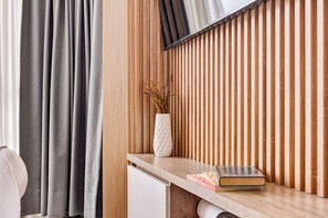 Ein Zimmer mit einer Wand aus Holzlamellen, einer weißen Vase mit Trockenpflanzen und einem Bücherregal aus Holz.