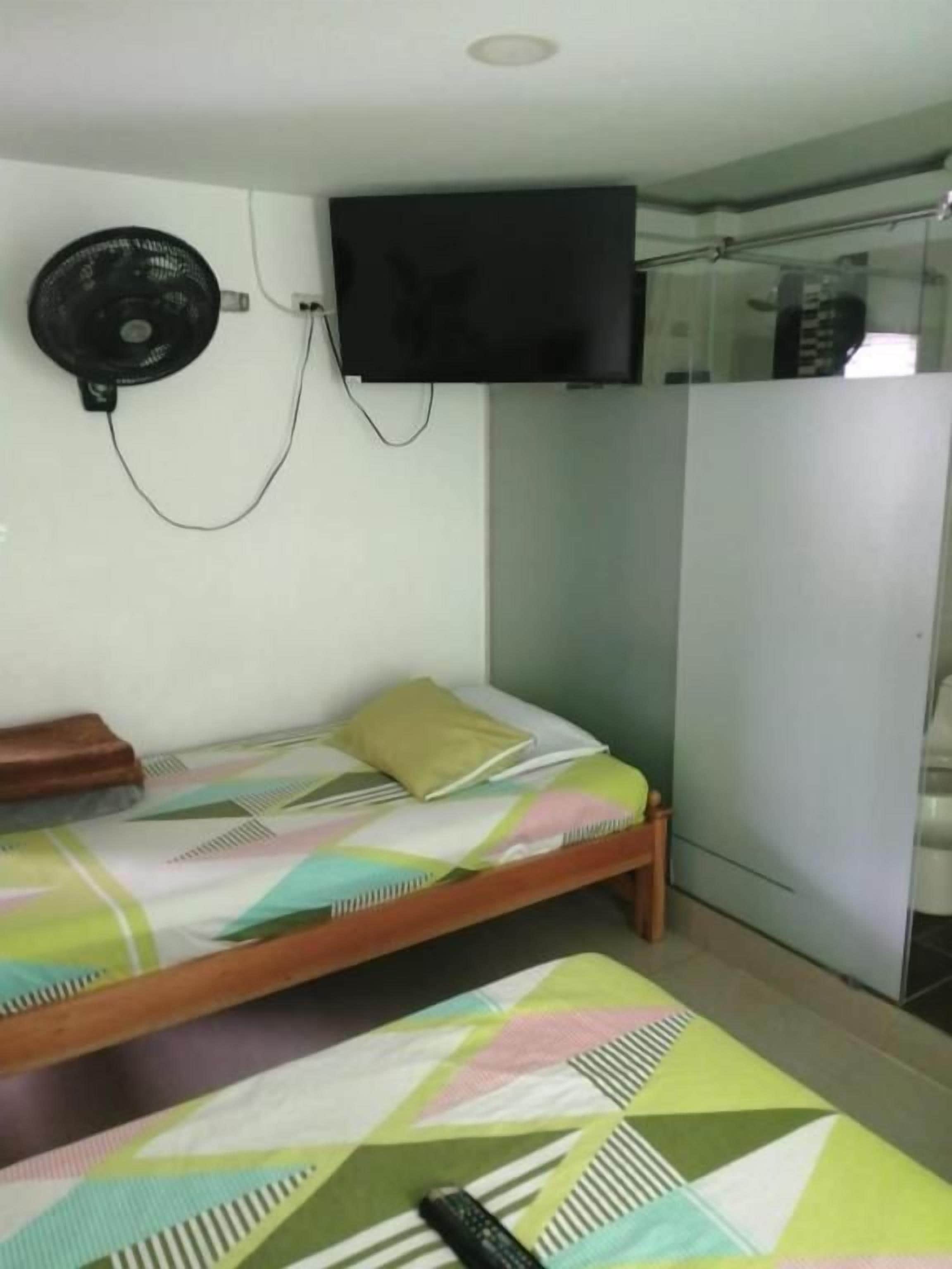 A room with a bed, a television mounted on the wall, and a fan.