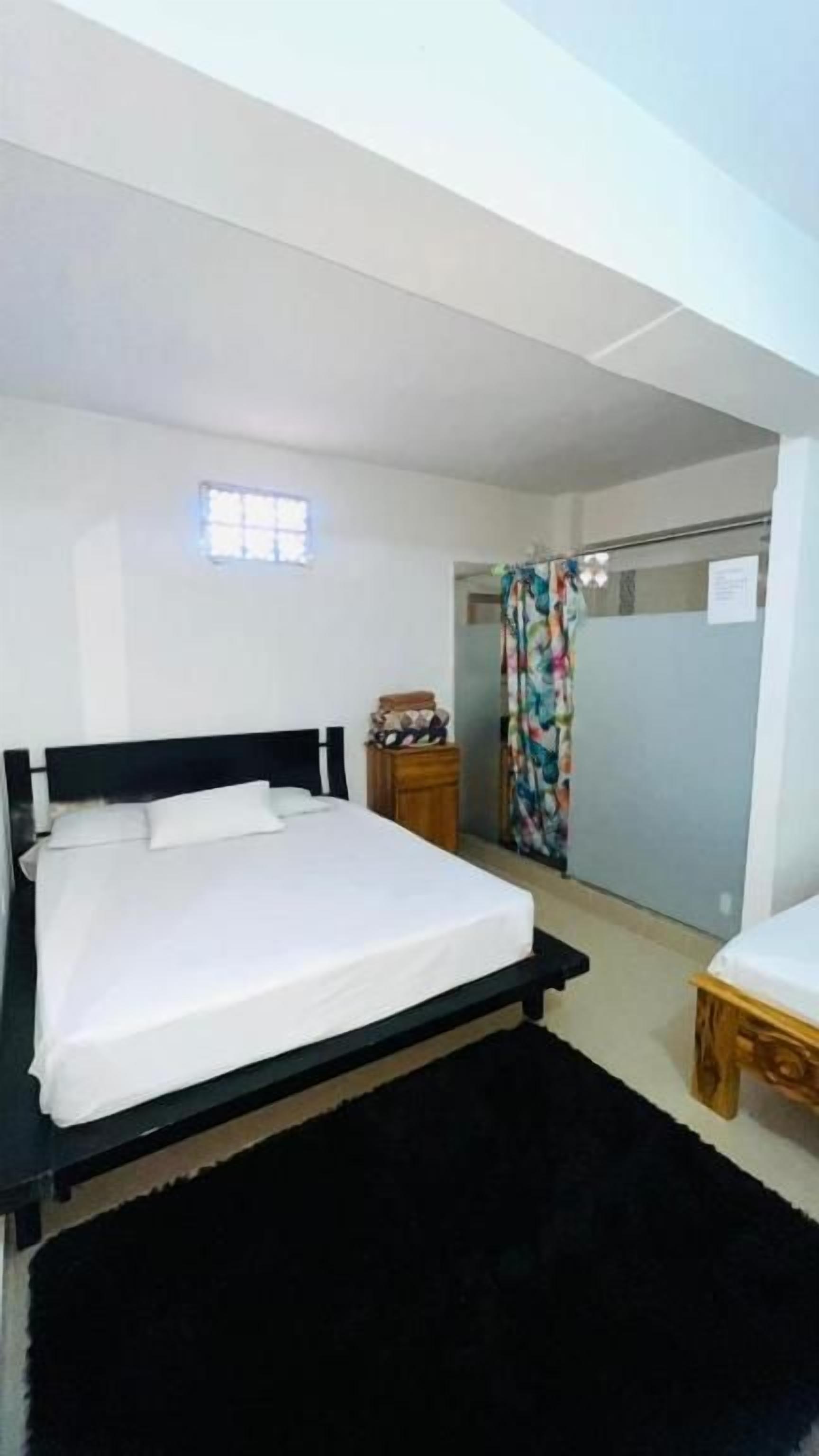 Un dormitorio con cama, una mesita, una mesita de noche, una ventana y una zona de ducha.