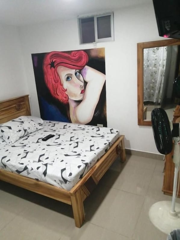 A bedroom with a bed, a painting, a mirror, and a desk.