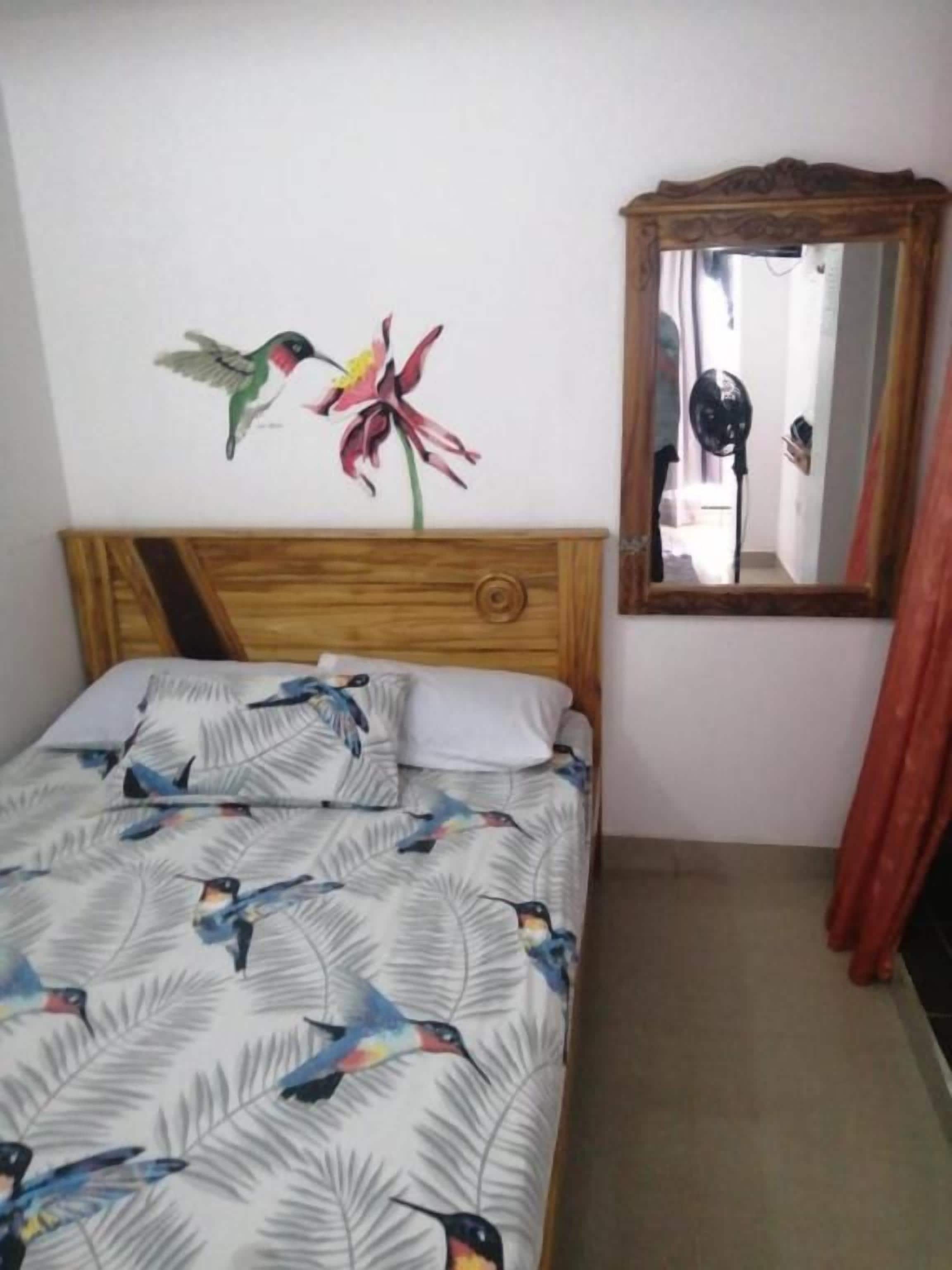 Ein Schlafzimmer mit einem Bett, einem Holzkopfstück, einem Spiegel und einer blumigen Wanddekoration.