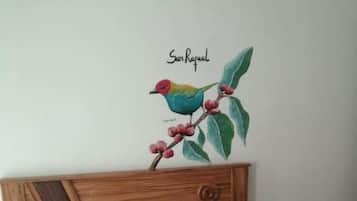 Un lit avec une couvre-lit à motifs géométriques, un oreiller vert à volants et une décoration murale représentant un oiseau coloré perché sur une branche.