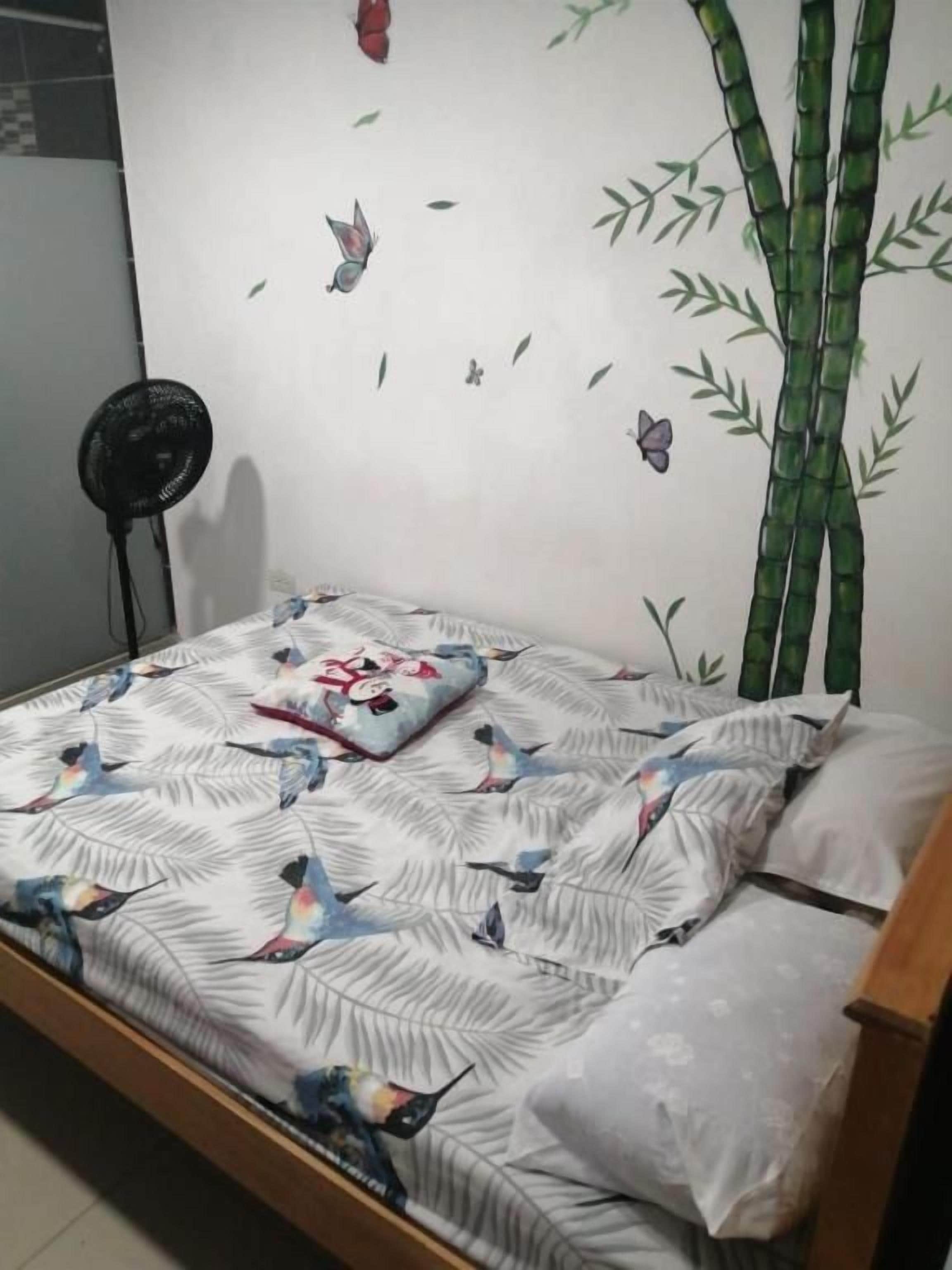 Un letto con copriletto decorato, un cuscino e una decorazione a parete con bambù e farfalle.