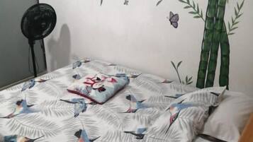 Un letto con copriletto decorato, un cuscino e una decorazione a parete con bambù e farfalle.