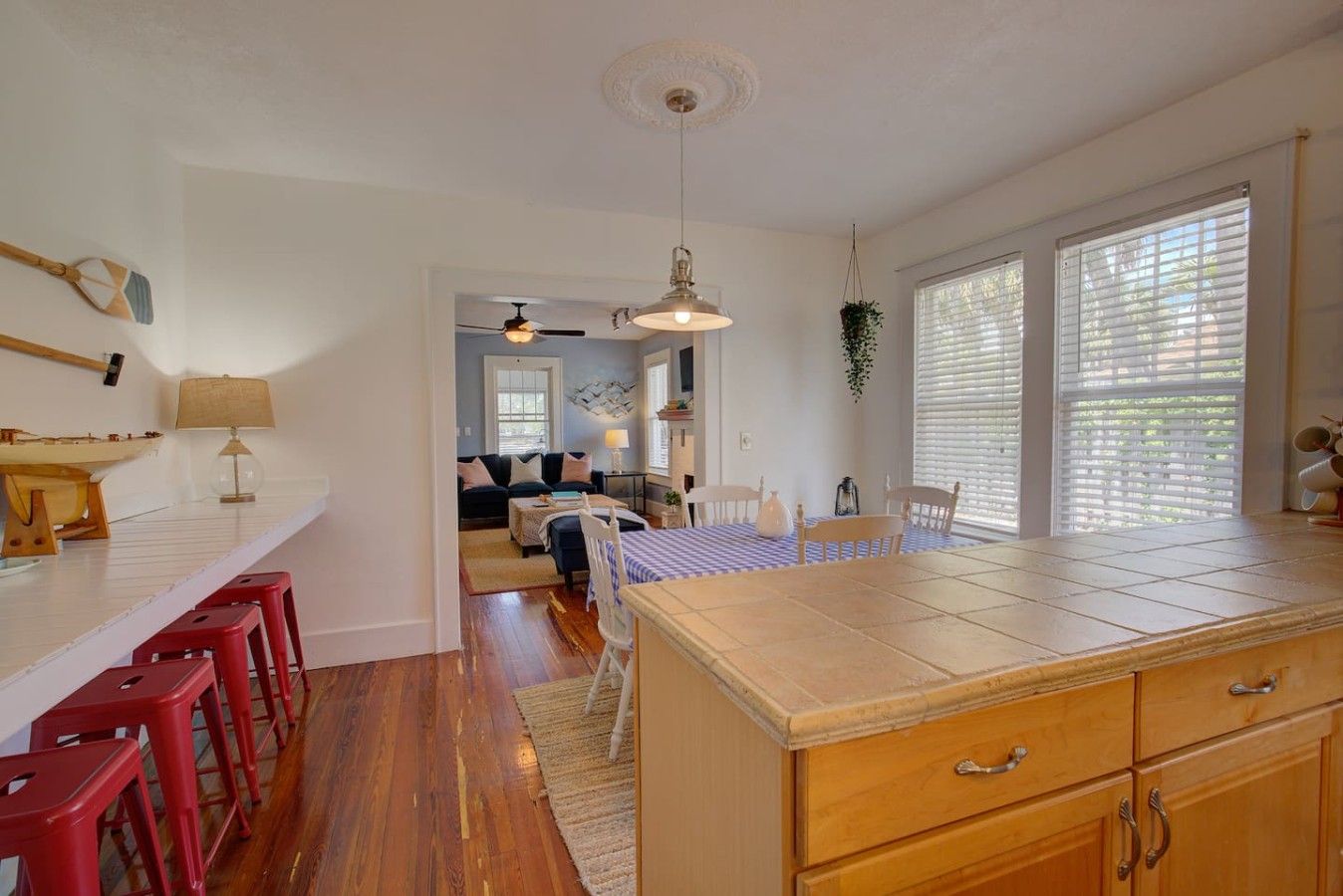 A kitchen with a central island, red bar stools, a dining table with chairs, and a ceiling fan.
