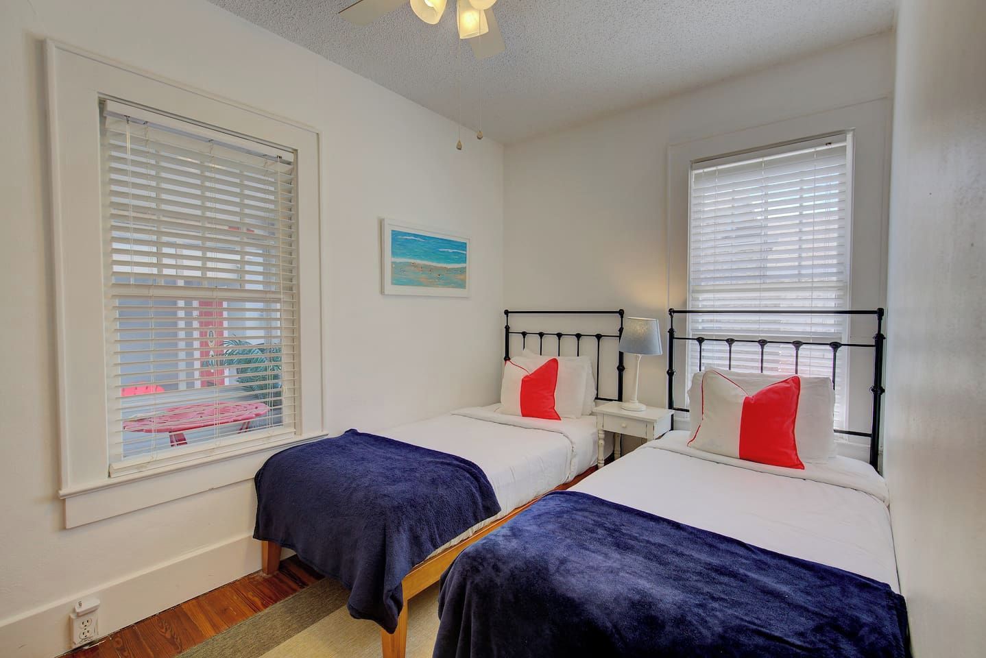 Een slaapkamer met twee eenpersoonsbedden, witte muren en een raam met zonwering.