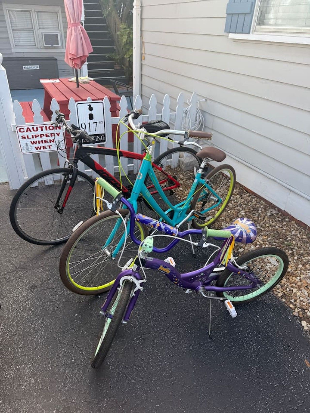 Three bicycles parked outside a house with a caution sign for slippery surfaces.