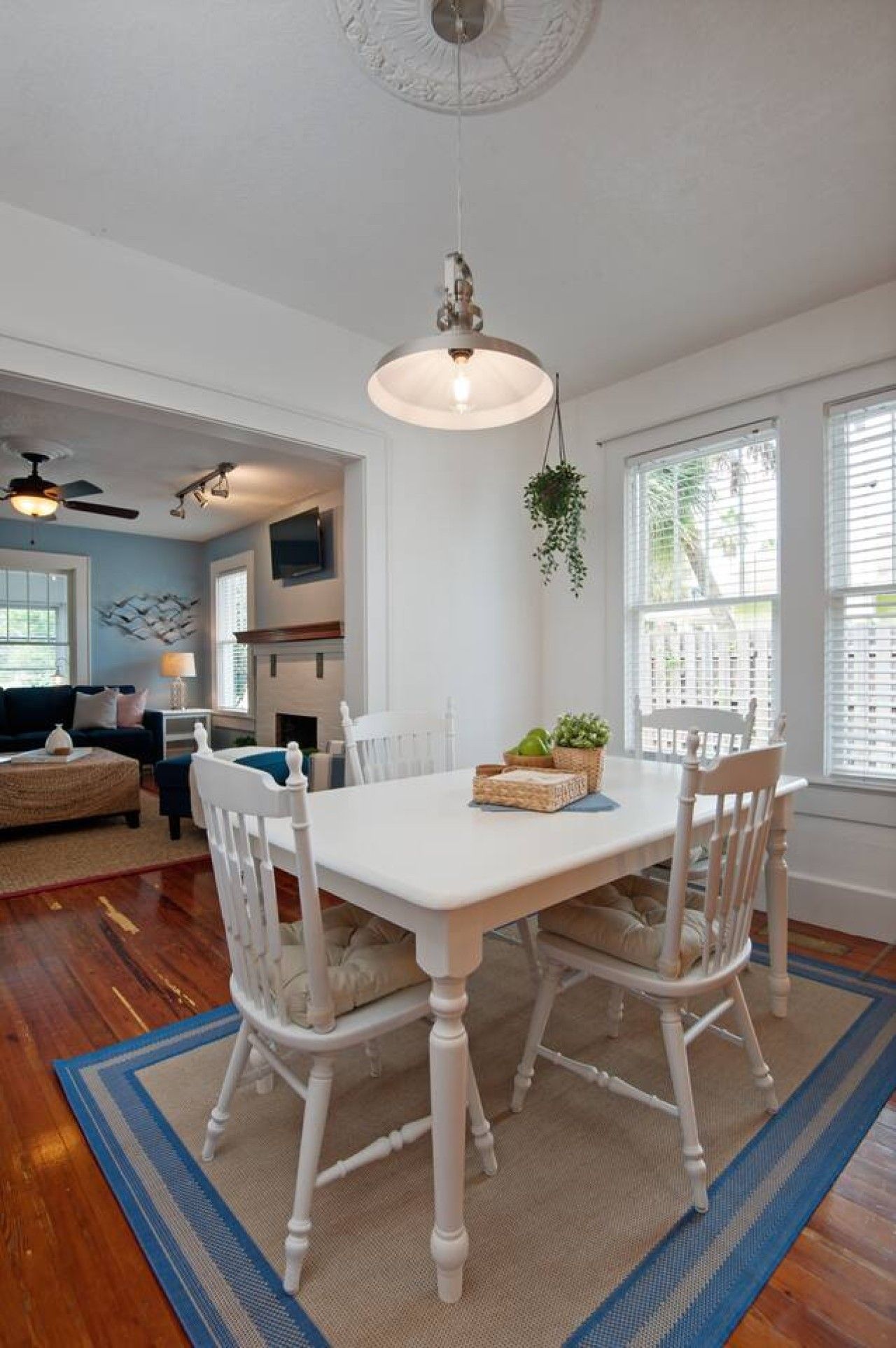 A dining area with a white table and chairs, a hanging light fixture, and a view of the living room.