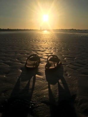 A pair of sandals on a beach with the sun setting in the background. - Beachy Modern Downtown Getaway I (Dunedin)