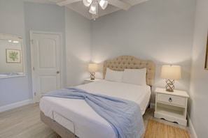 A bedroom with a bed, two bedside tables, a ceiling fan, a door, and a wall-mounted light fixture. - Beachy Modern Downtown Getaway I (Dunedin)