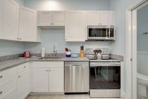 A modern kitchen with white cabinetry, stainless steel appliances, and a granite countertop. - Beachy Modern Downtown Getaway I (Dunedin)