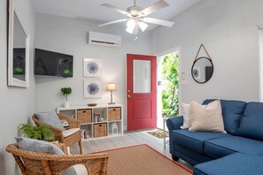 Una sala de estar con un sofá azul, sillas de mimbre, una puerta roja y un ventilador de techo.