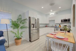 A modern kitchen with white cabinetry, stainless steel appliances, and a dining area with a wooden table and chairs. - Beachy Modern Downtown Getaway I (Dunedin)