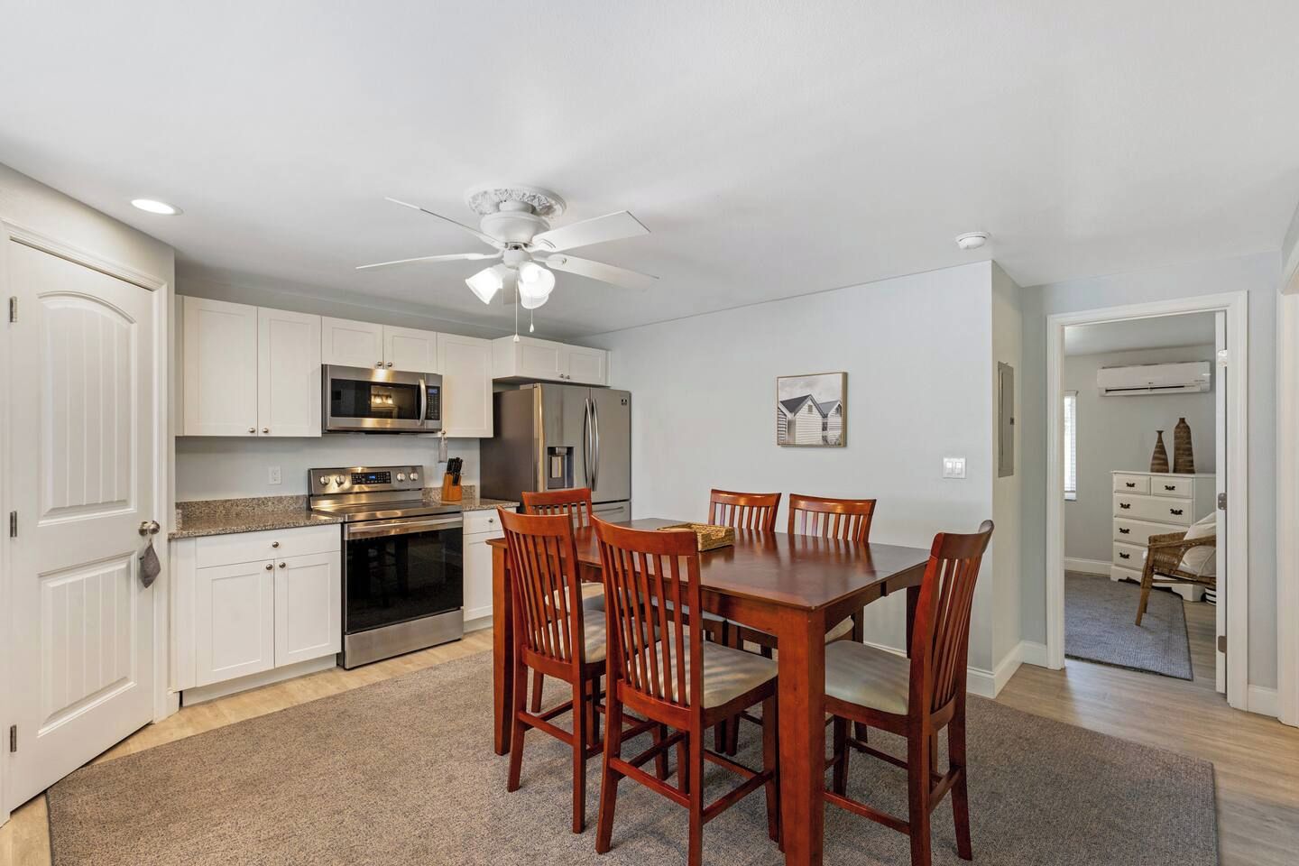 A modern kitchen with white cabinets, stainless steel appliances, and a dining area with wooden chairs.