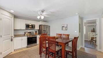 A modern kitchen with white cabinets, stainless steel appliances, and a dining area with wooden chairs.
