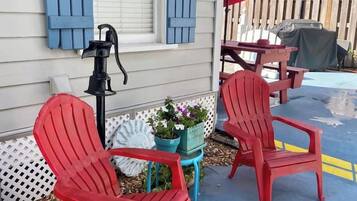 Two red Adirondack chairs, a small table, and a red umbrella outside a house with blue shutters.