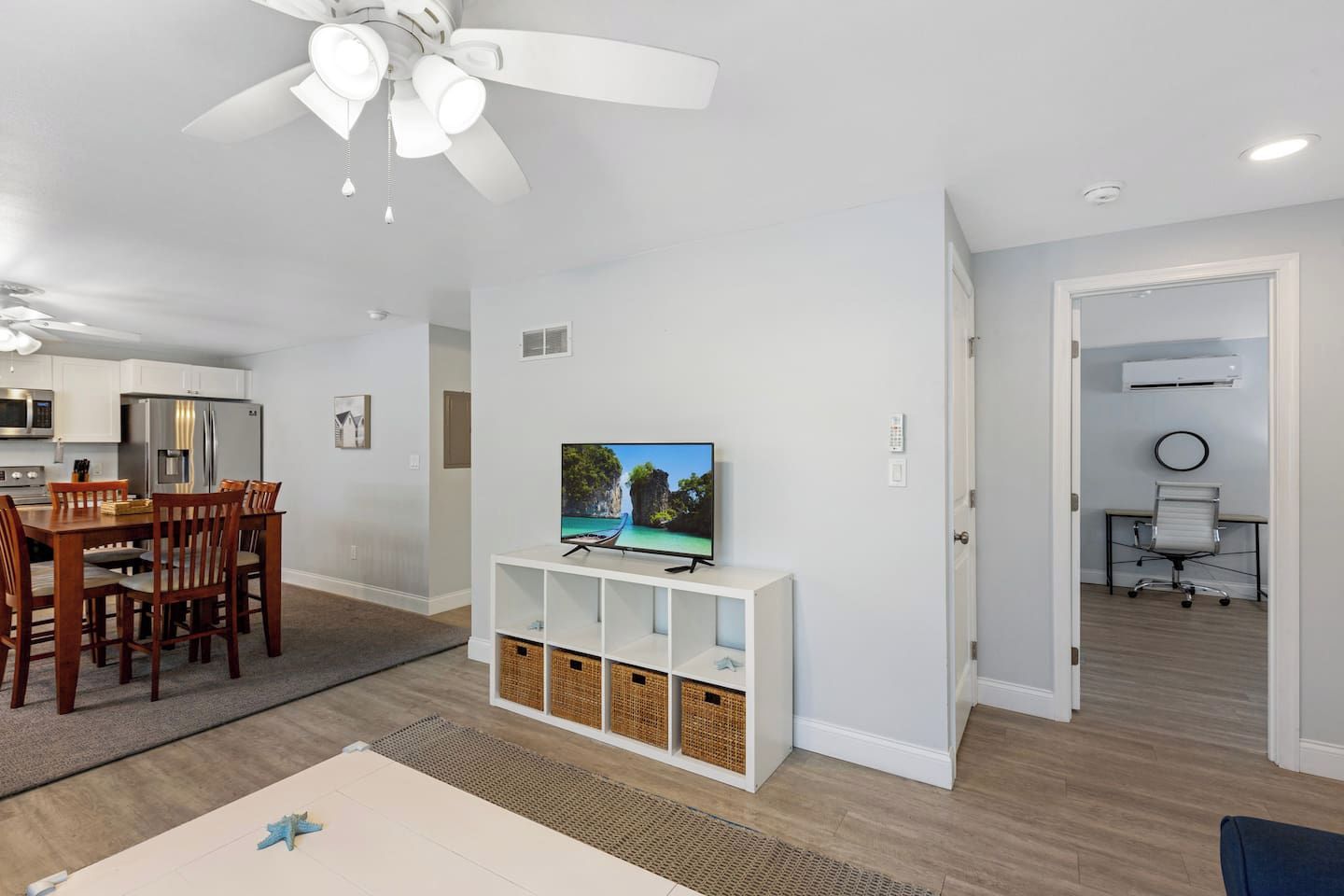 A modern living room with a dining area, a TV on a stand, and a ceiling fan.