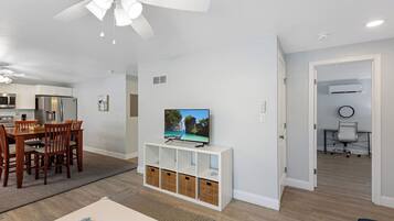 A modern living room with a dining area, a TV on a stand, and a ceiling fan.