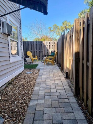 A patio area with a brick pathway, wooden fence, and two yellow chairs. - Downtown Dunedin 917-1/2 (Dunedin)