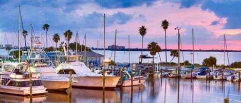 A marina with boats docked, calm water, and a bridge in the background.