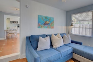 A living room with a blue sofa, a painting of a sea creature, and a window with blinds. - Downtown Dunedin 917-1/2 (Dunedin)