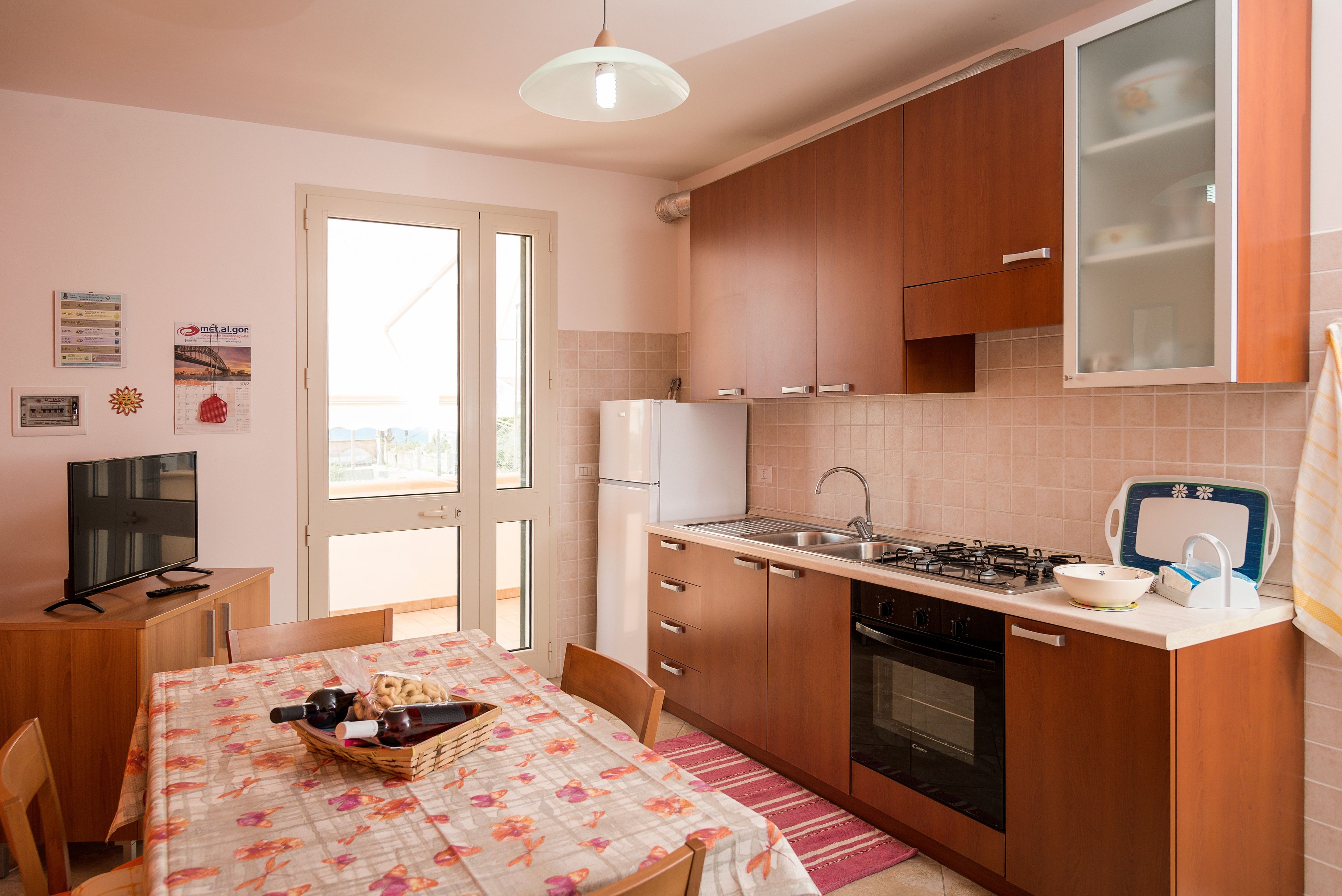 Cocina compacta con refrigerador, estufa y lavamanos. Hay una mesa de comedor con sillas y un televisor sobre un mueble de madera.