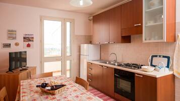 Cocina compacta con refrigerador, estufa y lavamanos. Hay una mesa de comedor con sillas y un televisor sobre un mueble de madera.