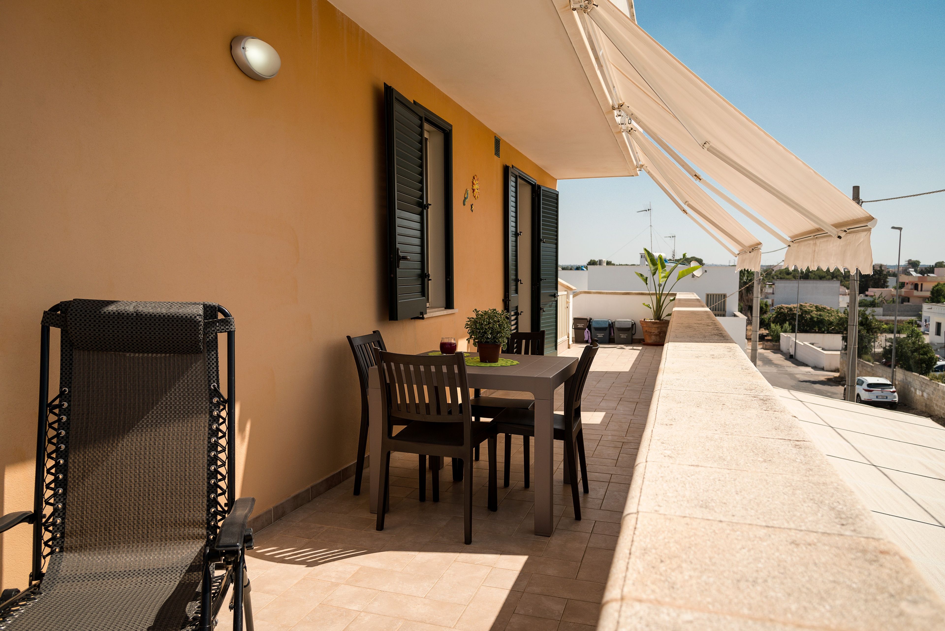 Une terrasse extérieure avec une table et des chaises, une plante en pot et un auvent blanc.