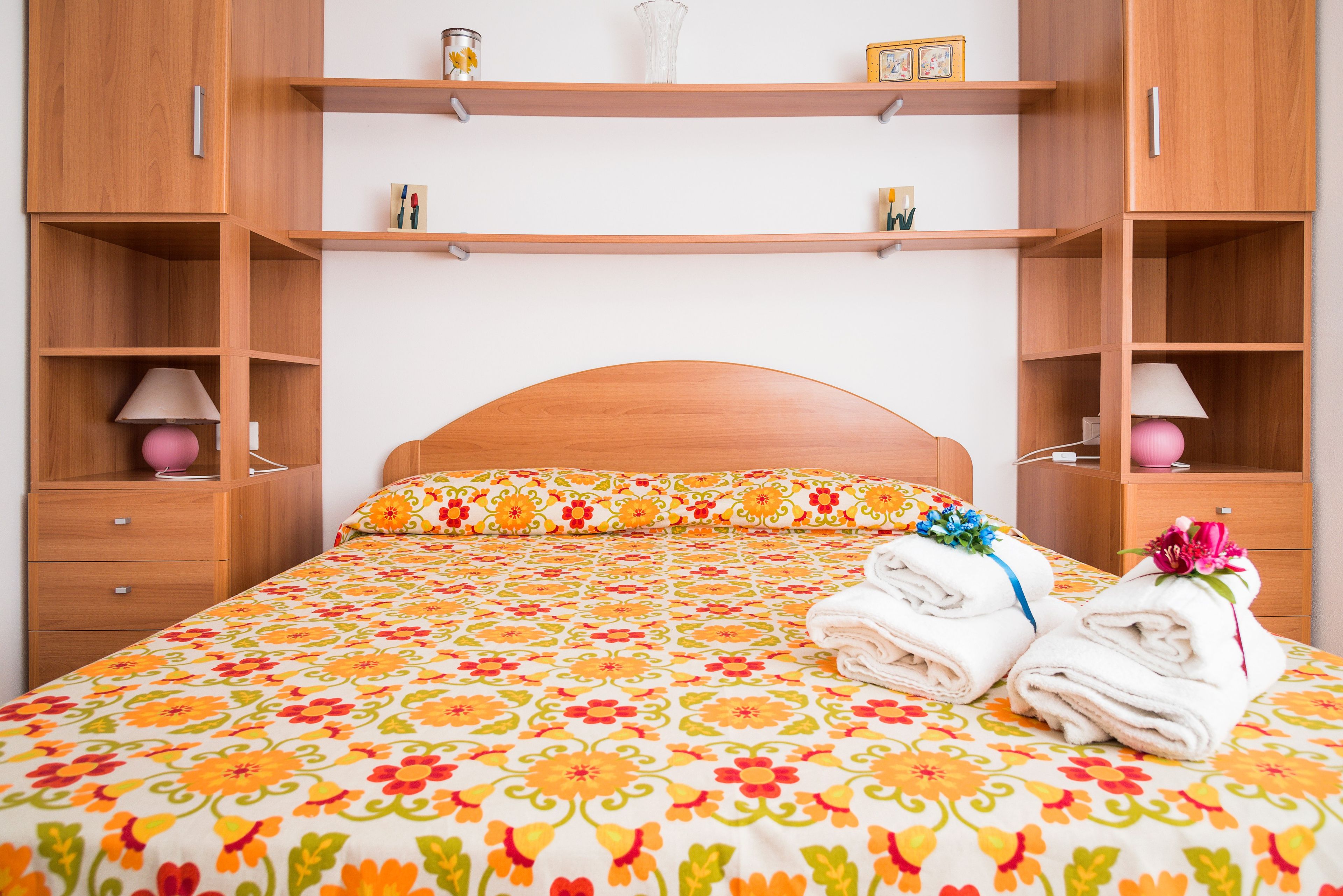 Un letto rifatto con una coperta a fiori, due lampade sui comodini e una pila di asciugamani piegati.