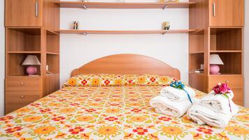 Un letto rifatto con una coperta a fiori, due lampade sui comodini e una pila di asciugamani piegati.