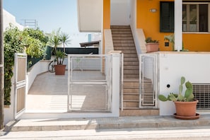 A residential building with a gated entrance, a staircase leading to an upper floor, and potted plants.
