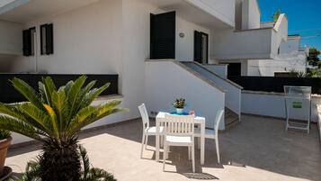 Eine Terrasse mit Tisch und Stühlen, einem Blumentopf und einer Treppe, die zu einer oberen Ebene führt.