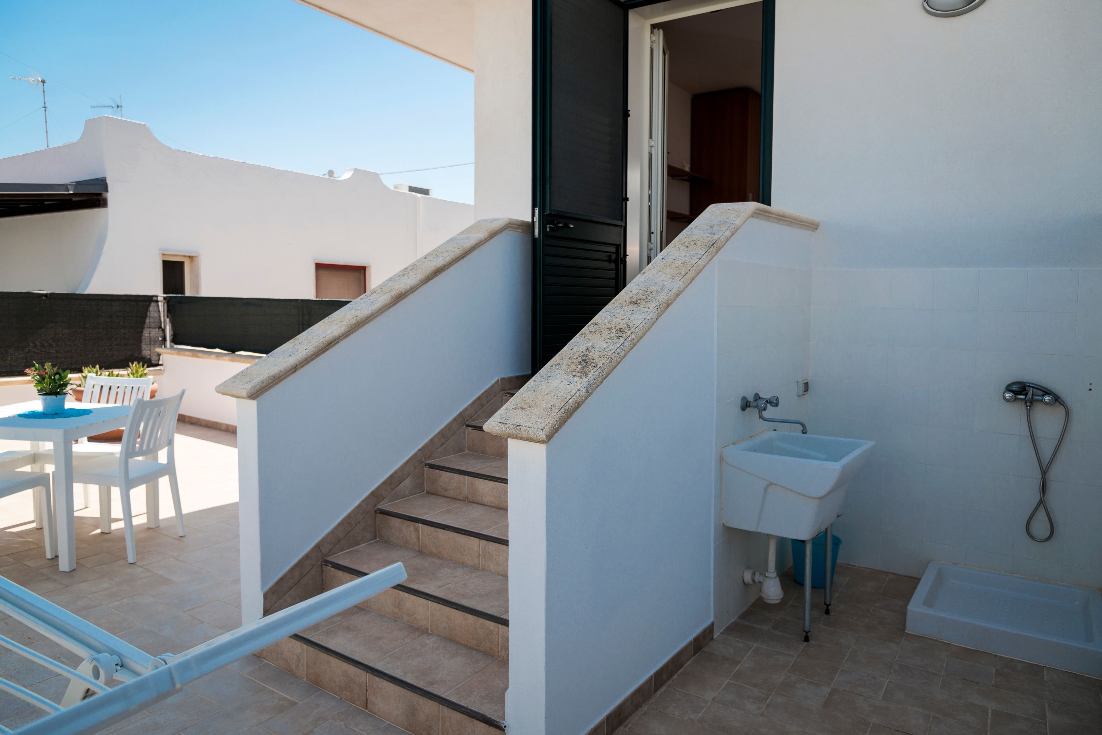 Un interior residencial con una escalera que lleva a un balcón, un baño pequeño con un lavamanos y un comedor con mesa y sillas.