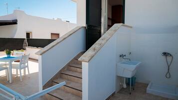 Un interior residencial con una escalera que lleva a un balcón, un baño pequeño con un lavamanos y un comedor con mesa y sillas.
